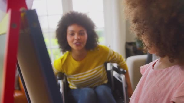 坐在轮椅上的母亲看着女儿在家里的白板上画着有趣的图画 动作缓慢 — 图库视频影像