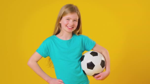 スタジオショットの笑顔の女の子を保持サッカーボール下腕と黄色のスタジオの背景にカメラを見て スローモーションで撮影 — ストック動画