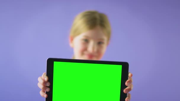 一个微笑的女孩拿着绿色屏幕的数码平板电脑 在紫色工作室的背景下看着相机的工作室照片 慢镜头 — 图库视频影像