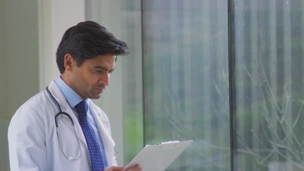 Male Doctor Wearing White Coat Standing Hospital Corridor Looking Clipboard — Stock Video