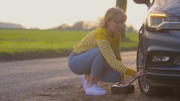 田舎道に電動ポンプ付きフラットカータイヤを膨らませる女性 スローモーションで撮影 — ストック動画