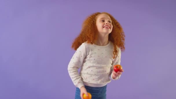摄影棚拍摄红头发少女在紫色摄影棚背景下杂耍苹果和橙子 慢镜头拍摄 — 图库视频影像