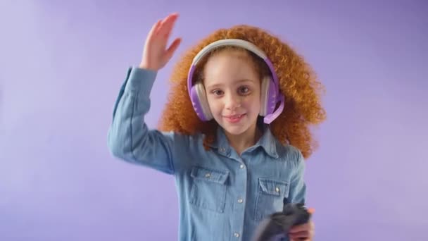 コントローラの背景とゲームヘッドセットを身に着けている赤い髪の少女のスタジオショット スローモーションで撮影 — ストック動画
