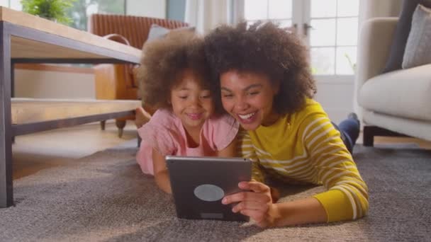 母と娘が楽しんで床の上に横たわっている一緒に自宅でデジタルタブレットで自画自慰のために面白い顔を引っ張る スローモーションで撮影 — ストック動画