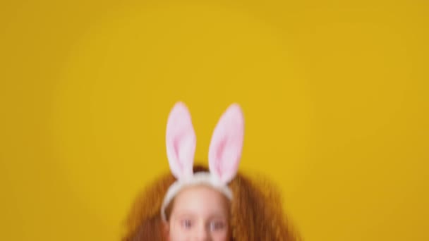 演播室拍摄的穿着兔子耳朵的女孩在黄色背景下从镜框底部跳了进来 动作缓慢 — 图库视频影像