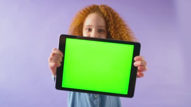 一个微笑的女孩拿着绿色屏幕的数码平板电脑 在紫色工作室的背景下看着相机的工作室照片 慢镜头 — 图库视频影像