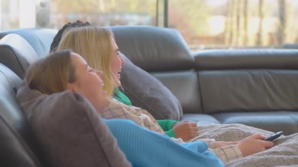 グループの多文化10代の女の子の友人に座ってソファの上で一緒にテレビを見て自宅で毛布の下に座って スローモーションで撮影 — ストック動画