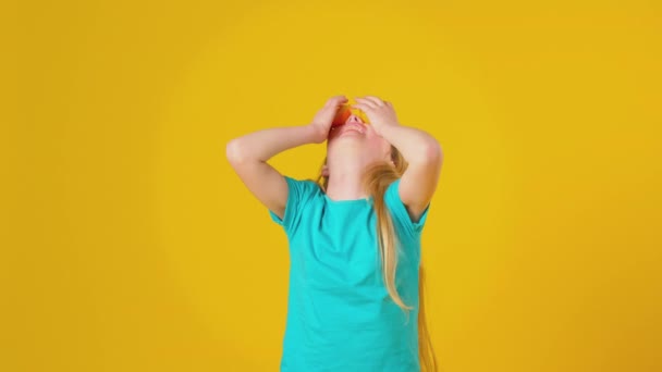 演播室里拍摄的女孩在脸前面平衡两半橙子的镜头 就像眼镜和黄色的演播室背景 动作缓慢 — 图库视频影像