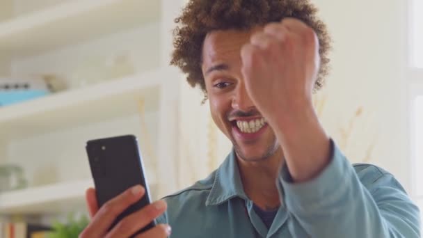 Celebrando Homem Casa Usando Telefone Celular Recebendo Boas Notícias Sobre — Vídeo de Stock