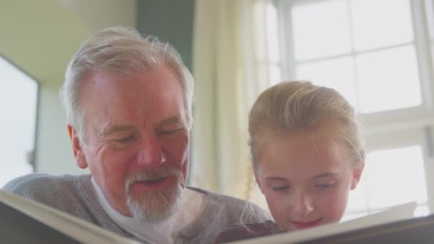 祖父のクローズアップと孫娘と一緒に家で椅子に座って一緒に家族の写真アルバムを見て スローモーションで撮影 — ストック動画