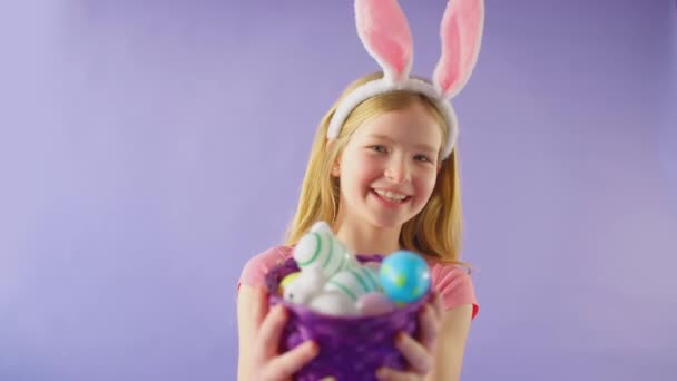 演播室拍摄的女孩戴着兔子耳朵 拿着一篮子紫色背景的复活节彩蛋 动作缓慢 — 图库视频影像