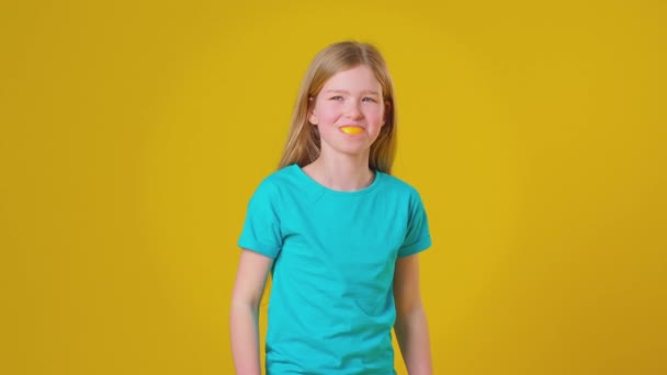 演播室拍摄的女孩使用橙色的部分作为嘴巴和牙齿在黄色的演播室背景下 慢动作拍摄 — 图库视频影像