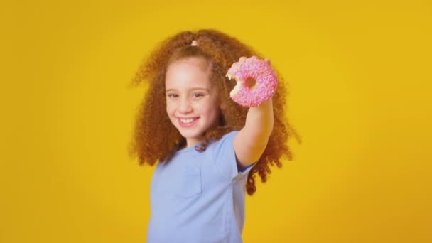 Estudio Niña Pelirroja Comiendo Donut Sobre Fondo Amarillo Disparo Cámara — Vídeos de Stock