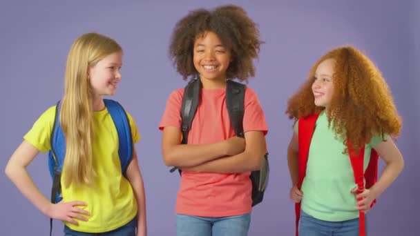 バックパックを着て紫を背景に学校に行く3人の子供のスタジオショット スローモーションで撮影 — ストック動画
