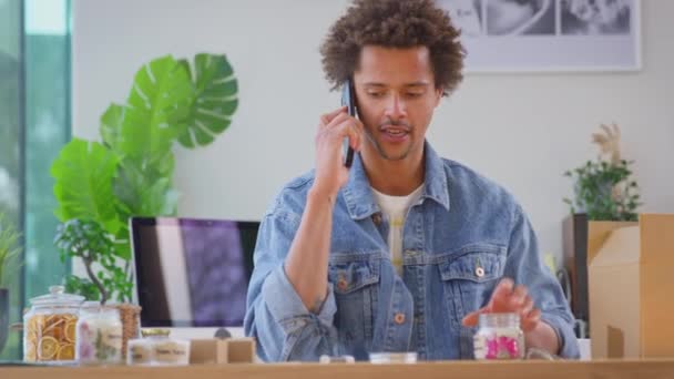 オンラインビジネスを実行している男は自宅で携帯電話で話してブティックキャンドルを作る スローモーションで撮影 — ストック動画