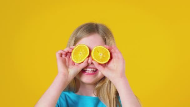 Estudio Niña Sosteniendo Dos Mitades Naranjas Frente Cara Como Gafas — Vídeos de Stock