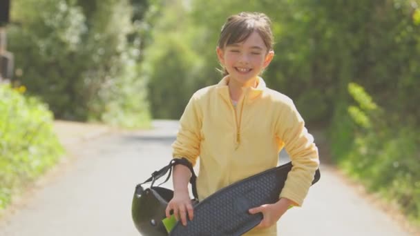 田舎道をスケートボードで歩く笑顔の女の子の肖像画 — ストック動画