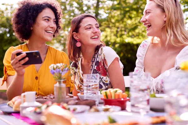 Three Female Friends Looking Photos Mobile Phone Eating Meal Outdoors — Stok fotoğraf