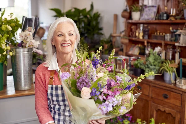 Female Owner Of Florists Shop Arranging Bouquet Of Flowers