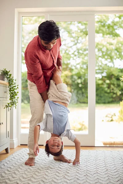 Father Holding Son Upside Down Playing Game In Lounge At Home Together