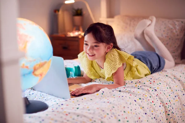 Girl In Bedroom At Night Lying On Bed Using With Laptop With Illuminated Globe