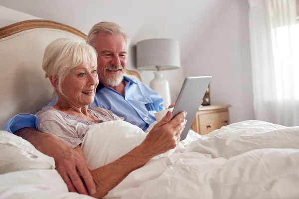 Retired Senior Couple In Bed At Home Using Digital Tablet