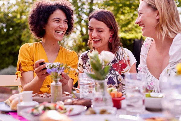 Three Female Friends Looking Photos Mobile Phone Eating Meal Outdoors — Stok fotoğraf