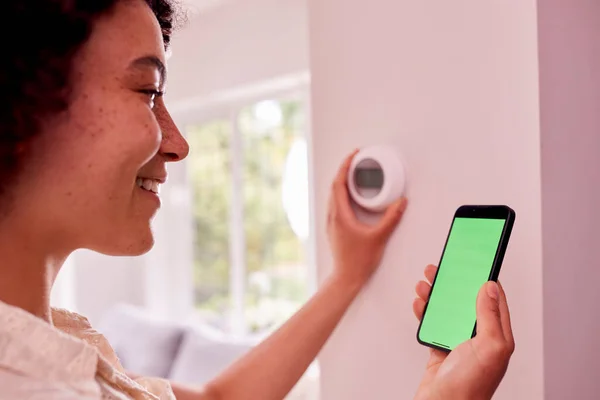 Close Up Of Woman With Green Screen On Mobile Phone To Control Central Heating Thermostat At Home