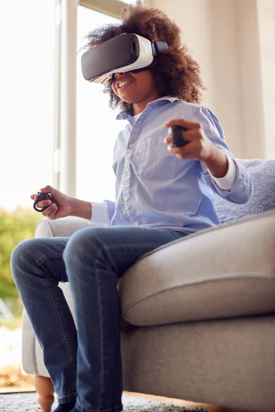 Boy Sitting On Sofa In Lounge Wearing VR Headset Playing Game
