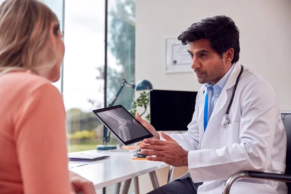 Doctor Wearing White Coat In Office Showing Mature Female Patient X-Ray Or Scan On Digital Tablet