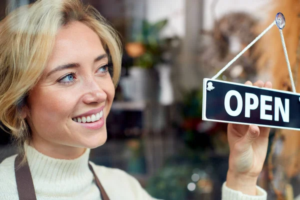 Smiling Female Owner Of Small Business Turning Round Open Sign In Shop Window