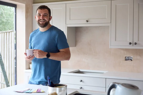 笑顔の男の肖像 自宅でキッチンを改装コーヒーブレイクでペイント時計を見て — ストック写真