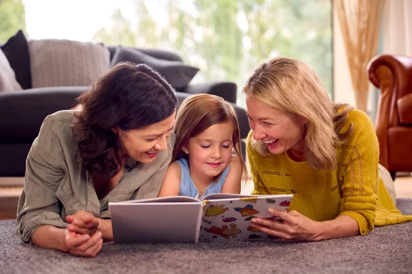 2人のママと娘が一緒に家で読書本に横たわっているのと同じセックス家族 — ストック写真