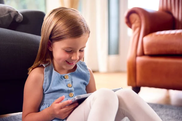 自宅の若い女の子は ラウンジの床に座ってゲームをプレイしたり デジタルタブレットで映画を見て — ストック写真