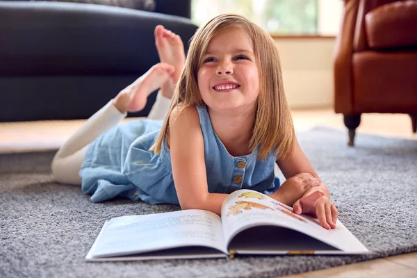 家にいる若い女の子は読書本の床に横たわっています — ストック写真