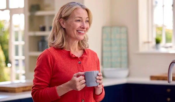 Gülümseyen Olgun Bir Kadın Mutfakta Kahve Fincanıyla Dinleniyor — Stok fotoğraf