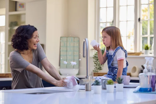 有女儿的家庭帮助年迈的母亲在厨房里洗碗 在家里吹泡泡肥皂 — 图库照片