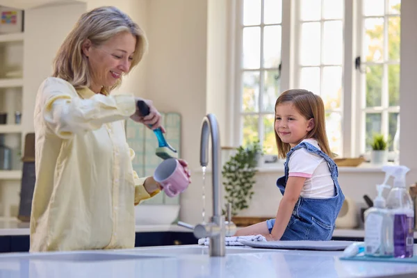 お母さんが家で台所で洗濯するのを手伝ってくれる娘を持つ家族 — ストック写真