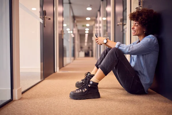 年轻的女商人坐在现代办公室走廊的地板上 用电话微笑 — 图库照片