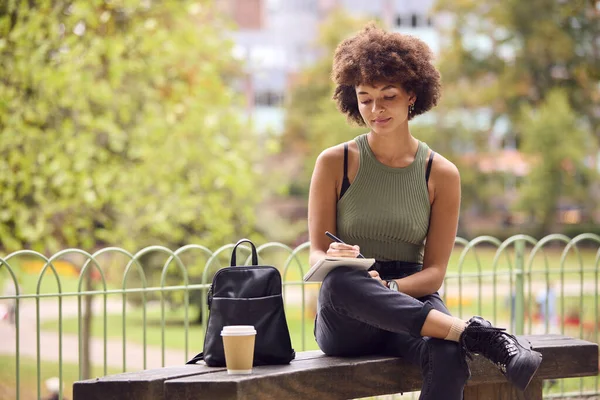 stock image Young Woman Outdoors In Park Sitting On Bench Working Writing In Notebook