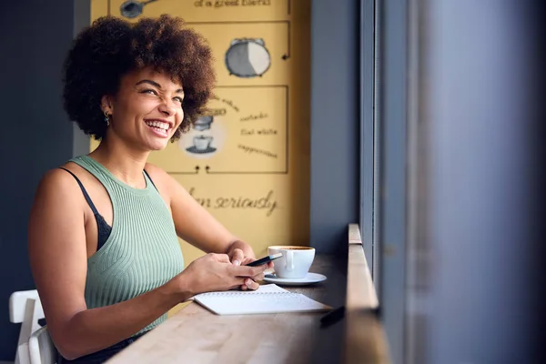 咖啡店橱窗中的女性顾客使用移动电话上网工作 — 图库照片