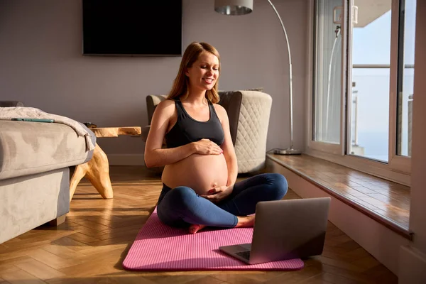 在网上瑜伽课上 怀孕妇女穿着手提电脑的健康服装在家做运动 — 图库照片