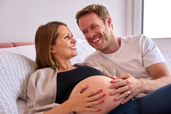 妊娠中の女性の胃に触れる男とベッドに横たわっ自宅でカップルを愛し — ストック写真