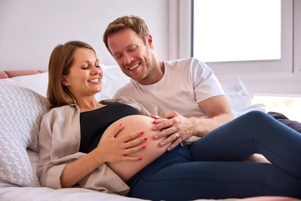 妊娠中の女性の胃に触れる男とベッドに横たわっ自宅でカップルを愛し — ストック写真