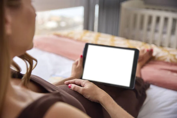 妊娠中の女性が自宅でベッドでリラックスグリーンスクリーンデジタルタブレットを見ながら胃を保持 — ストック写真