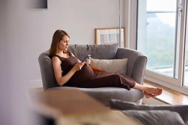 Беременная Женщина Мобильным Телефоном Отдыхает Диване Холдинге Живот — стоковое фото