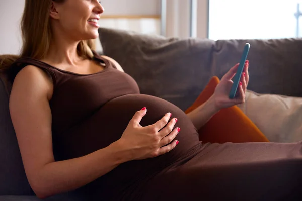 Zbliżenie Kobiety Ciąży Telefonu Komórkowego Relaks Kanapie Domu Gospodarstwa Żołądka — Zdjęcie stockowe