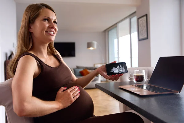 Kobieta Ciąży Pracuje Domu Laptopie Patrząc Telefon Usg Dziecka — Zdjęcie stockowe