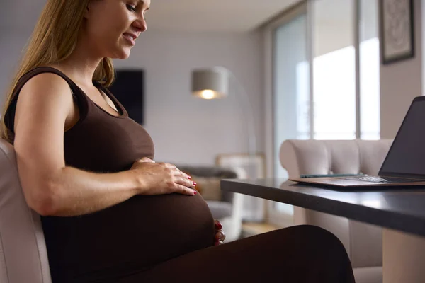 怀孕妇女在家中坐在手提电脑上 坐在桌旁 手忙脚乱 — 图库照片