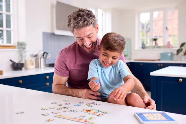 息子と一緒にジグソーパズルをやってキッチンで自宅で成熟したお父さん — ストック写真